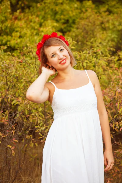 Schöne Frau mit einem Kranz roter Blumen auf einem Feld im Freien — Stockfoto