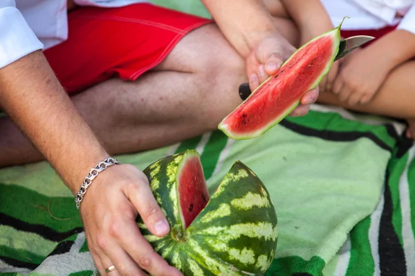 Man snijdt de watermeloen in segmenten. Picknick in het park buiten — Stockfoto