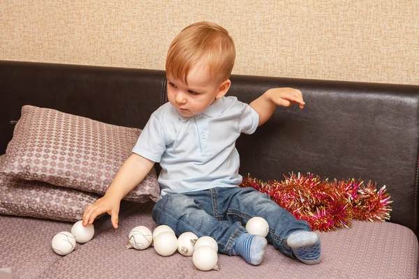 Small child playing with Christmas balls sitting on the couch — Stock Photo, Image
