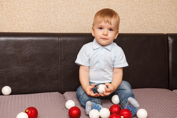 小さな子供がソファに座ってクリスマス ボールで遊んで — ストック写真