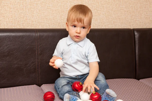 小さな子供がソファに座ってクリスマス ボールで遊んで — ストック写真