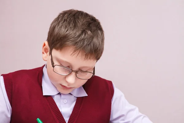 Niño con gafas sentado en un escritorio de escritura —  Fotos de Stock