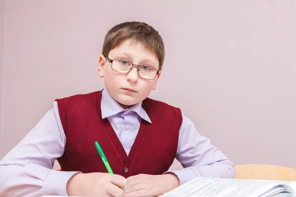 Мальчик в очках сидит за письменным столом и пишет — стоковое фото