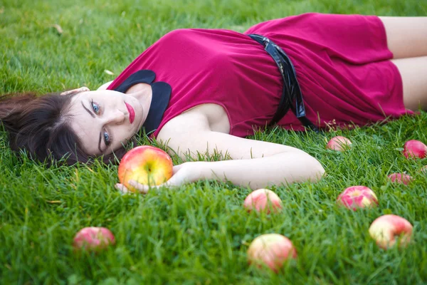 Hermosa mujer posando mientras está acostada en el césped con manzanas —  Fotos de Stock