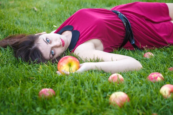 Hermosa mujer posando mientras está acostada en el césped con manzanas —  Fotos de Stock