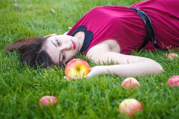 Hermosa mujer posando mientras está acostada en el césped con manzanas —  Fotos de Stock
