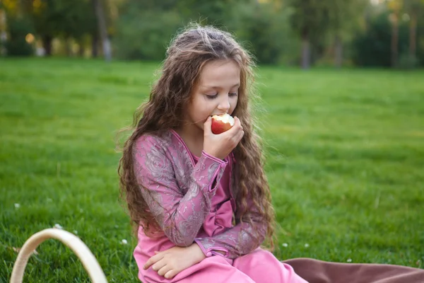 Ragazza che mangia una mela in un parco estivo seduta su un plaid — Foto Stock