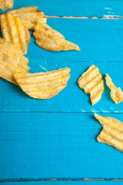 Potato chips scattered on a blue wooden table — Stock Photo, Image