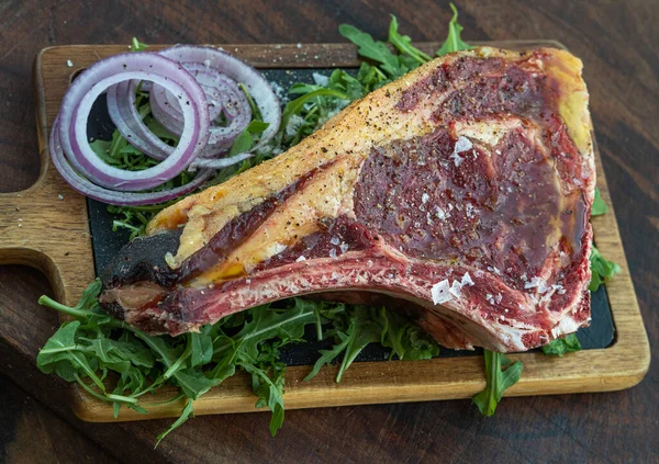 Bife preto angus cru em uma placa de madeira com salada de cebola e foguete — Fotografia de Stock