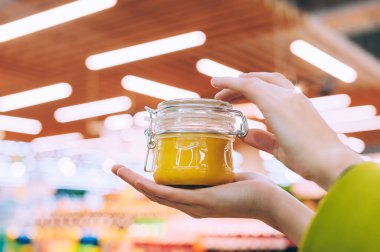 Süpermarkette bir kız elinde bal dolu cam bir kavanoz tutuyor. Lambaların arka planına karşı