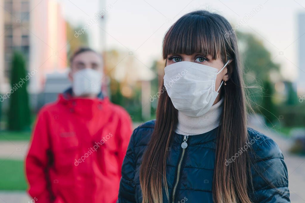 A girl in a medical mask is standing at a distance from people in the city