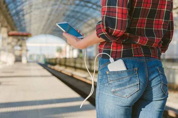 Tren istasyonundaki kız telefonu elektrik bankasından şarj ediyor.