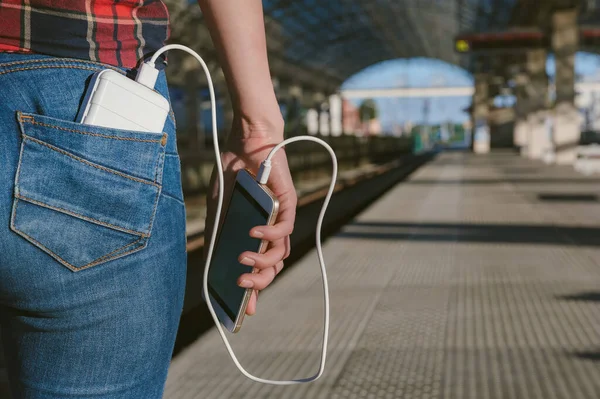 Tren istasyonundaki kızın arka cebindeki güç bankası akıllı telefondan para alıyor.