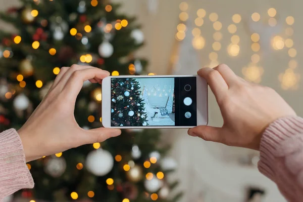 girl shoots photo video on smartphone mockup. Against the background of New Year and Christmas holidays, a cozy interior with a decorated Christmas tree