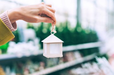 Kız elinde Noel ağacında süslemeleri olan dekoratif bir ev tutuyor. Mağazadaki yılbaşı dekorunun arka planına karşı.