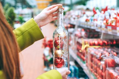 Kız elinde Noel ve yeni yıl için dekoratif toplarla dolu bir şişe tutuyor. Mağazanın arka planına karşı