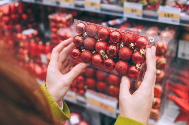 Kız Noel ve yeni yılı süslemek için elinde dekoratif kırmızı toplar tutuyor. Süpermarket tezgahının arka planında
