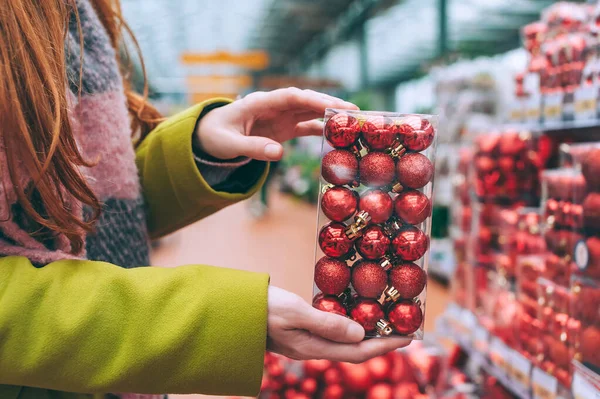 The girl holds decorative red balls in her hands to decorate Christmas and New Year. Against the background of the store