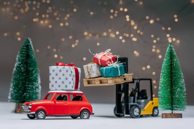 Bir Forklift kamyonu kırmızı arabaya hediyeler yükler. Yeşil ağaçların ve şenlikli ışıkların arka planına karşı. Noel ve Yeni Yıl teması kavramı