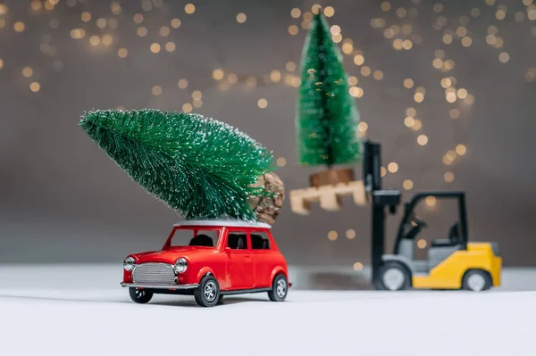 Bir yükleyici ve kırmızı retro manina yeşil ağaçlar taşıyor. Şenlik ışıklarının arka planına karşı. Noel ve Yeni Yıl teması kavramı