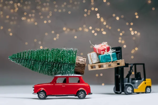 A loader loads gifts onto a Red Car with a Christmas tree on the roof. Against the background of festive lights