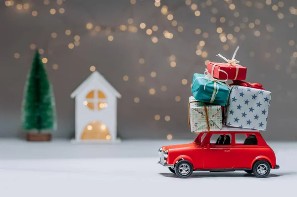 Çatıda hediyeler olan kırmızı bir araba. Bir evin arka planına ve bir Noel ağacına karşı. Noel ve Yeni Yıl teması kavramı