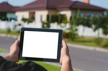 Bir adamın elindeki tablet, bir evin arka planına karşı.