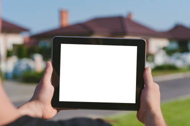 Evin arka planında, bir adamın elindeki tabletin yakın plan görüntüsü.