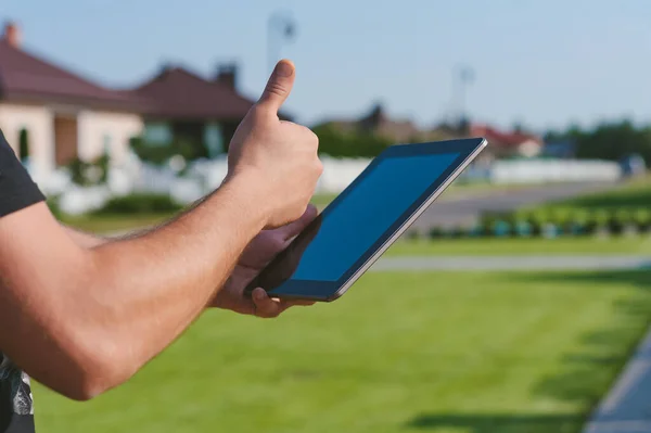 Finger in front of the Tablet on the background of the house