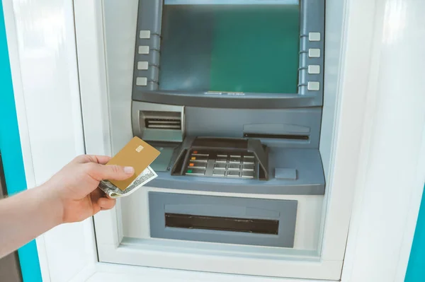 The guy holds money and a bank card in his hand in front of an ATM machine