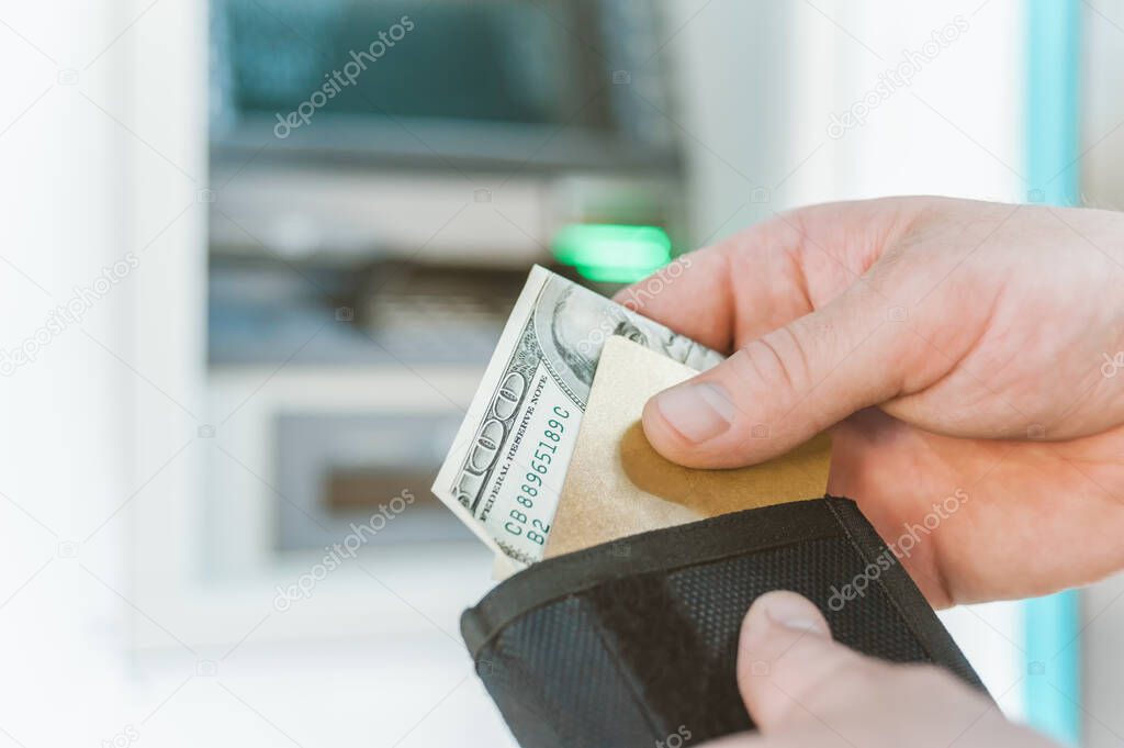 The man takes out a bank card with money from his wallet. Against the background of an ATM