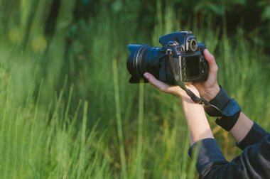 Yakın plan, profesyonel bir fotoğraf makinesi bir kızın elinde. Yeşil doğa ve ormanın arka planına karşı