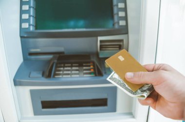 Yakın plan, bir adam elinde paralı bir banka kartı tutuyor. Bir ATM 'nin arka planında