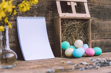 Üzerinde saman ve defter olan renkli yumurtalar. Eski bir tahtanın arka planında. Paskalya Günü temasına ilişkin kavram
