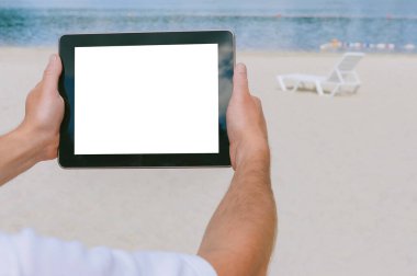 Kapatın. Tableti erkek eliyle hazırlayın. Sahilin ve şezlongların önünde