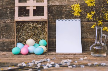 Üzerinde saman ve defter olan renkli yumurtalar. Eski bir tahtanın arka planında. Paskalya Günü temasına ilişkin kavram