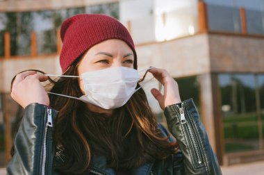 Kız yüzündeki tıbbi maskeyi çıkartıyor. Bir cam iş merkezinin arka planında