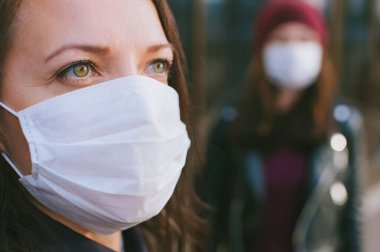 Başka bir kızın arka planında tıbbi maskeli bir kızın yakın plan portresi.