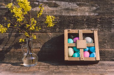 Bir vazo çiçekli masanın üstündeki bir kutuya yumurta boyamış. Eski tahtaların arka planına karşı. Paskalya temasına ilişkin kavram