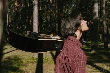 Elinde gitarla ormanda yürüyen bir adamın portresi. Ağaçların arka planına karşı
