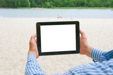 Tableti bir adamın ellerinde taklit et. Sahilin ve nehrin arka planına karşı.