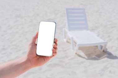 Erkek eliyle akıllı telefon taklidi yap. Sahilin ve şezlongların önünde