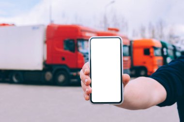 Bir adamın elinde akıllı bir telefon taklidi yap. Kırmızı kamyonların arka planına karşı. Lojistik kavramı