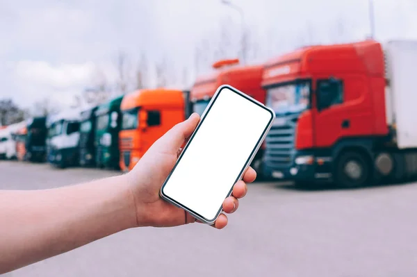 Bir adamın elinde akıllı bir telefon taklidi yap. Kırmızı kamyonların arka planına karşı. Lojistik kavramı
