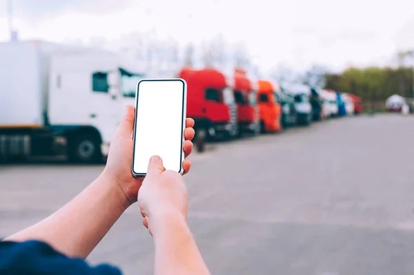 Bir adamın elinde akıllı bir telefon taklidi yap. Kırmızı kamyonların arka planına karşı. Lojistik kavramı