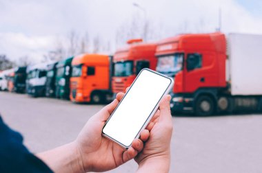 Bir adamın elinde akıllı bir telefon taklidi yap. Kırmızı kamyonların arka planına karşı. Lojistik kavramı