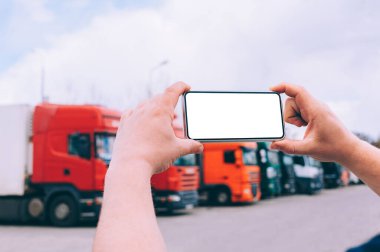 Bir adamın elinde akıllı bir telefon taklidi yap. Kırmızı kamyonların arka planına karşı. Lojistik kavramı