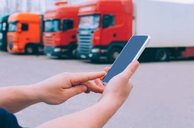 Bir adamın elinde akıllı bir telefon taklidi yap. Kırmızı kamyonların arka planına karşı. Lojistik kavramı