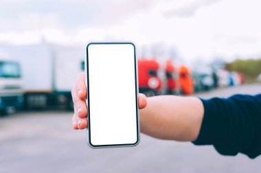 Bir adamın elinde akıllı bir telefon taklidi yap. Kırmızı kamyonların arka planına karşı. Lojistik kavramı
