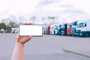 Bir adamın elinde akıllı bir telefon taklidi yap. Kırmızı kamyonların arka planına karşı. Lojistik kavramı